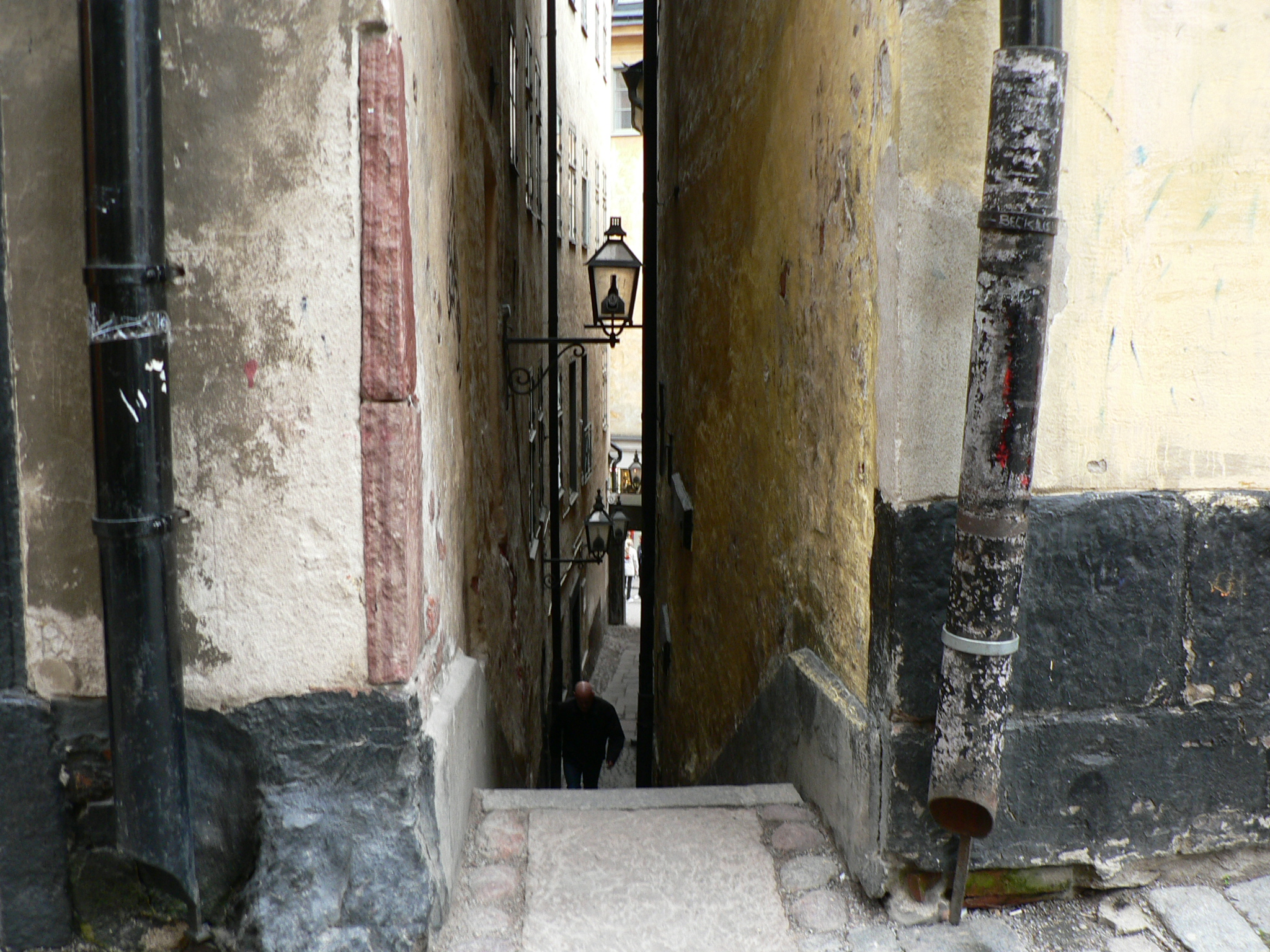 The narrow stepped alley of Mårten Trotzigs Gränd, its ochre and grey walls close on both sides, steps climbing up toward a slit of sky.