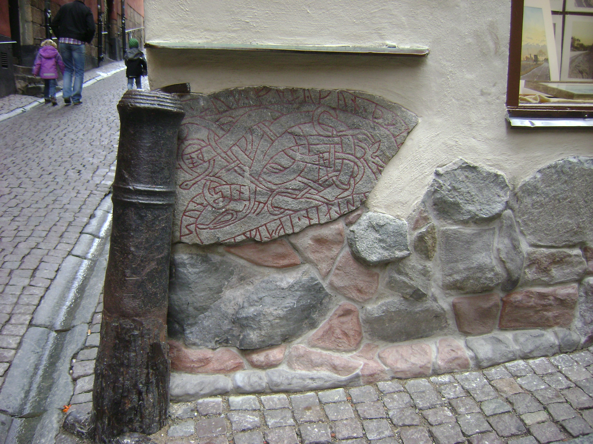 Runestone U 53, a carved granite stone with a winding serpent, set on its side into the corner foundation of a building.